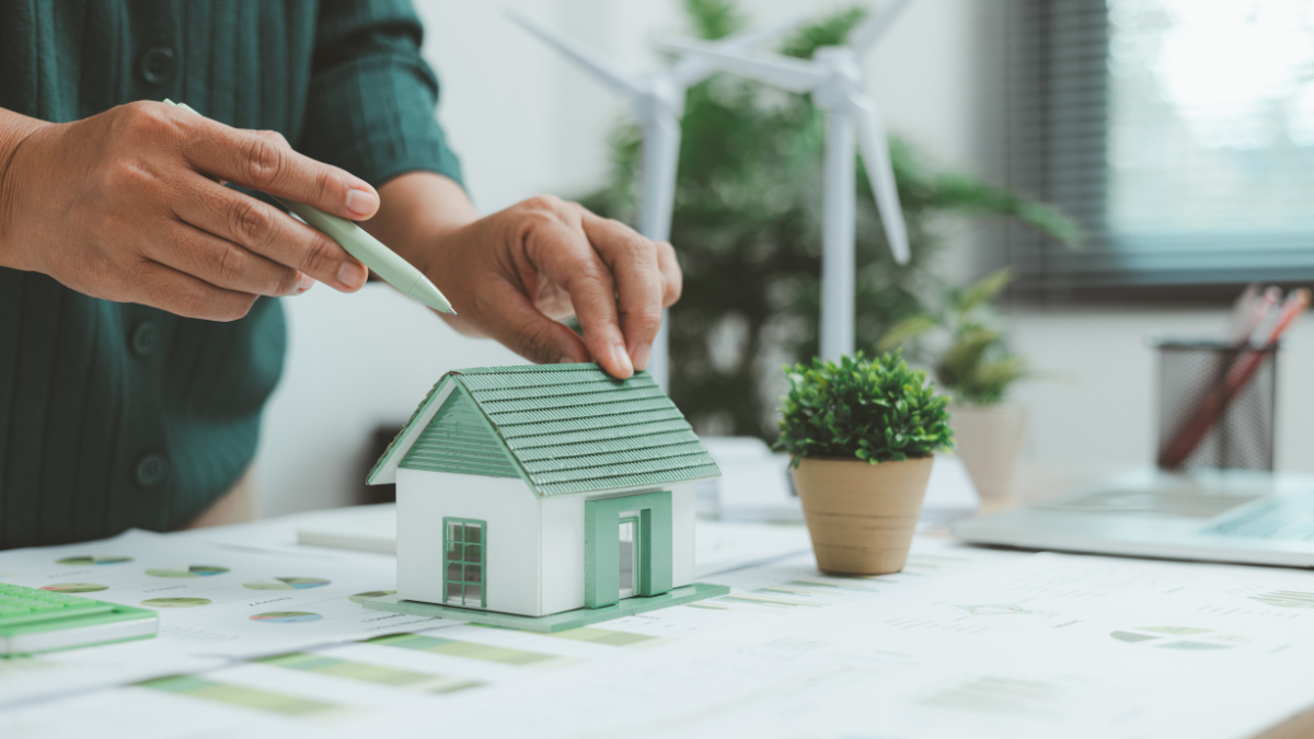 Homme avec une chemise verte tenant un stylo vert, devant une maquette de maison verte